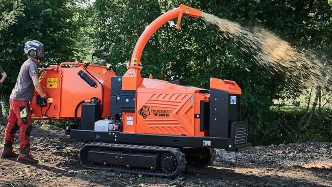 Beltegående flishugger i arbeid som kutter greiner og spruter flis ut i naturen.